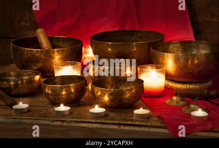 Ciotole cantanti tibetane con candele accese su sfondo rosso Foto Stock