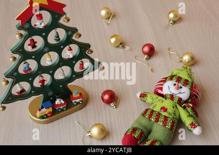 Pupazzo di neve ripieno e giocattolo per l'albero di Natale su sfondo in legno per le festività di dicembre. Baule natalizie, decorazioni per la stagione invernale in rosso e oro Foto Stock