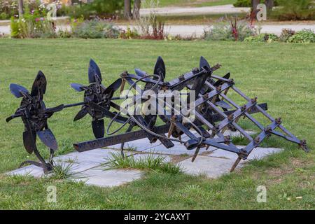 Vecchi macchinari agricoli arrugginiti esposti su prato verde nel parco. Concetto di strumenti agricoli d'epoca e attrezzature per lo stile di vita rurale Foto Stock