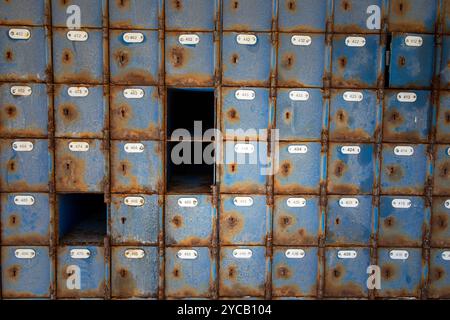 Grandi quantità di cassette postali blu arrugginite in un ufficio postale abbandonato. Ad alcune scatole mancano le porte. Foto Stock