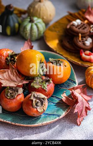 Un'esibizione festosa di prelibatezze di Halloween che presentano i cachi d'arancia su un piatto di ceramica, circondati da mini zucche, biscotti con condimento al marshmallow e vib Foto Stock