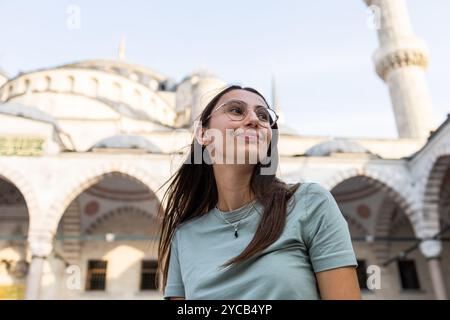 Una giovane donna gode di una giornata di sole visitando la Moschea Blu o Sultanahmet Camii a Istanbul, guardando lontano con un'espressione gioiosa. Foto Stock