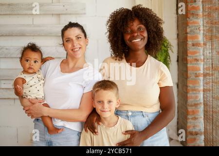 Famiglia multirazziale unita in un ambiente accogliente e sorridente davanti alla telecamera. Il gruppo comprende una donna afroamericana, una donna caucasica Foto Stock