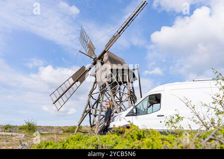 Scopri la Scandinavia in un viaggio su strada attraverso l'isola di Oland, Svezia. Questa immagine mostra una giovane donna in piedi accanto a un tradizionale mulino a vento, con un minuto Foto Stock