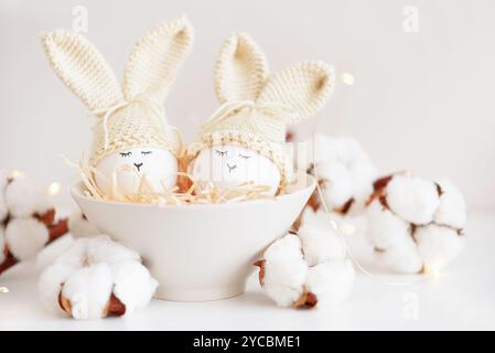 Uova di Pasqua in cappelli a maglia con orecchie di coniglio nel nido. Concetto di festa di Pasqua Foto Stock