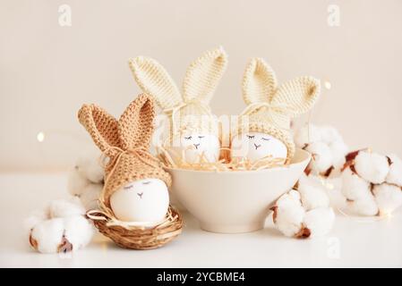 Uova di Pasqua in cappelli a maglia con orecchie di coniglio nel nido. Concetto di festa di Pasqua Foto Stock