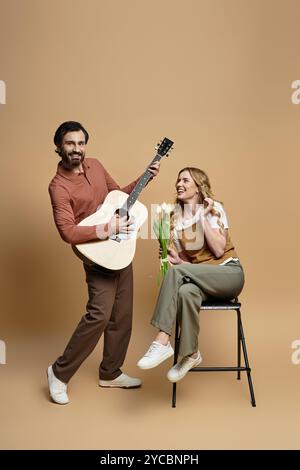 Un uomo allegro suona la chitarra mentre una donna sorride con fiori freschi, diffondendo gioia. Foto Stock