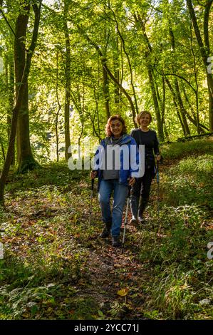 Due donne di mezza età camminano lungo un pendio su una collina boscosa, con la luce del sole su foglie verdi brillanti a South Downs nel West Sussex, Inghilterra. Foto Stock