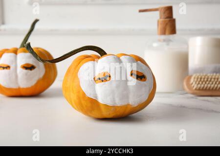 Zucche con maschere in argilla, pennello e prodotti cosmetici su tavola grunge bianca su sfondo in legno Foto Stock