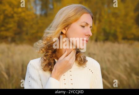 Giovane donna malata stanca affetta da mal di gola acuto, tocca il collo con la mano, si sente male all'aperto nel parco autunnale, stagione autunnale Foto Stock