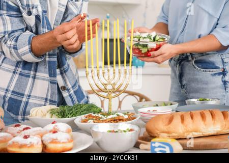 La famiglia felice accende le candele sul tavolo da pranzo servito nella cucina festosa. Festa Hanukkah Foto Stock