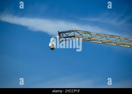 Una telecamera di sorveglianza è posizionata in modo prominente su una struttura alta, catturando immagini da un alto punto panoramico sotto il cielo azzurro Foto Stock