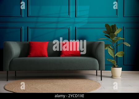 Comodo divano con cuscini e piante d'casa vicino alla parete color tè in camera Foto Stock