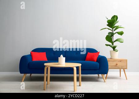 Comodo divano blu, tavoli e piante d'casa vicino alla parete grigia in camera Foto Stock