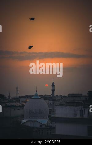 L'alba colora il cielo in calde tonalità di arancio e pesca, mentre gli uccelli si innalzano aggraziatamente verso la tranquilla moschea, accogliendo un nuovo giorno. #Sunrise #Mosq Foto Stock