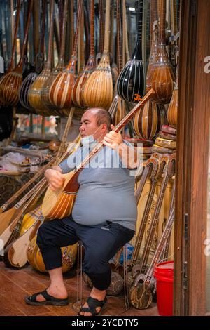 Kashgar, Cina - 17 LUGLIO 2022: Uomo uiguro seduto e suonando strumenti uiguri tradizionali nel suo negozio di strumenti musicali in un mercato locale nella vecchia Ka Foto Stock