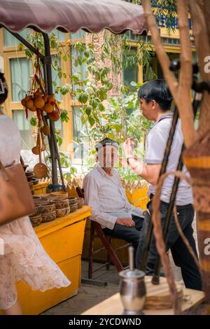 Kashgar, Cina - 17 LUGLIO 2022: Uomo uiguro seduto nel suo tradizionale negozio di legno uiguro in un mercato locale nella vecchia Kashgar Foto Stock