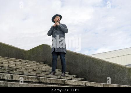 Ritratto di un giovane elegante e affascinante con un cappotto all'aperto. Un uomo che indossa un cappotto e una sciarpa che guarda lontano e si chiede Foto Stock