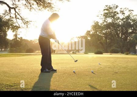 Uomo adulto che gioca a golf al tramonto Foto Stock