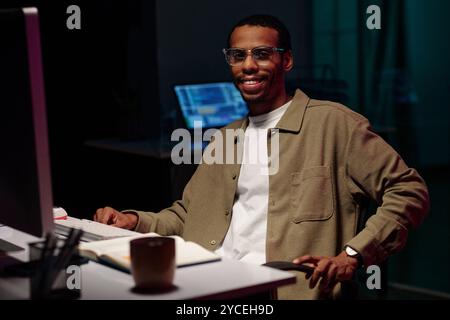 Uomo sorridente che lavora al computer in ambiente Dark Office Foto Stock