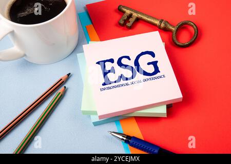 Governance sociale ambientale ESG. Blocco note con testo, tazza da caffè e chiave dorata sul tavolo dell'ufficio. Foto Stock