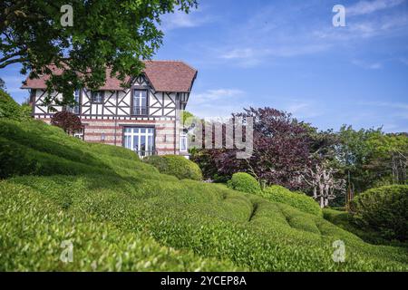 Stupendo panorama dei giardini Etretat (così chiamato giardino) in questo villaggio di Etretat, Normandia. Grande albero con foglie rosse e cespugli topiari e casa in distan Foto Stock