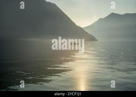 Paesaggio fiabesco sul lago di Como con barca di pescatori e piccolo corpo di sagoma di pescatore in lontananza in inverno nel nord Italia. Quasi visibile Foto Stock