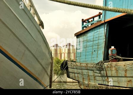 Edifici torreggianti sulla zona costiera di Giacarta sono visti attraverso le barche phinisi al porto tradizionale Sunda Kelapa a Giacarta, Indonesia. Foto Stock