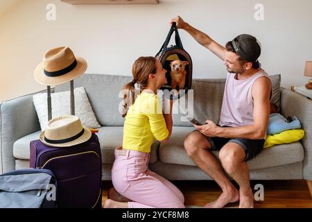 Giovane coppia a casa che si prepara a viaggiare con il loro piccolo cane in un portabagagli. Foto Stock