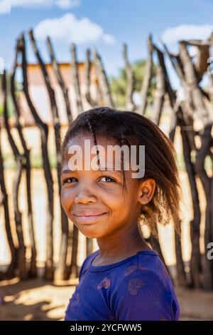 Bambina africana single del villaggio in piedi nel cortile di fronte alla recinzione di legno Foto Stock