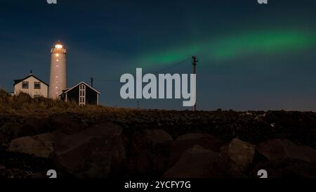 Faro illuminato di notte con sottile boreale verde aurora, Islanda Foto Stock