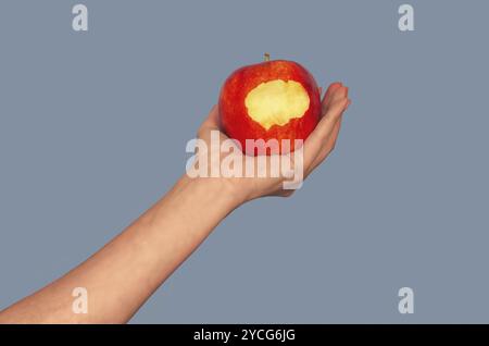 Mordere la mela sul palmo della donna su sfondo grigio. Mela come simbolo di frutta proibita, piacere Foto Stock