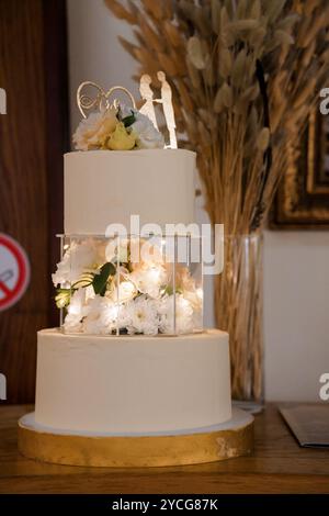 Elegante torta nuziale a tre piani adornata con fiori freschi e toppa romantica. Foto Stock