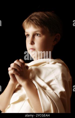 Giovane ragazzo in uniforme implorando o pregando Foto Stock