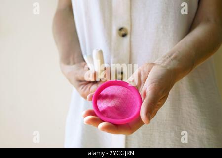 Una donna regge un disco mestruale con una mano e un paio di tamponi di cotone nell'altra. Rifiuto di prodotti igienici monouso Foto Stock