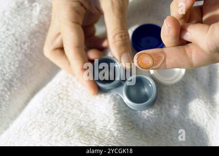 Correzione della visione: Una donna prende una lente a contatto colorata da un contenitore, foto da vicino. Un dito femminile con una lente a contatto riutilizzabile appoggiata su di esso Foto Stock