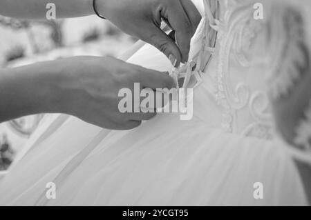 Damigella aiutando slanciata allacciatura sposa il suo matrimonio abito bianco, abbottonatura sul delicato merletto pattern con mantello soffice sulla vita. Mattina prepara nuziale Foto Stock