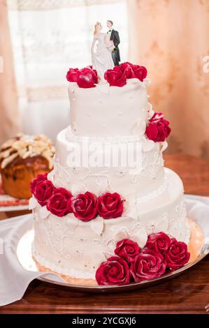 Elegante torta nuziale a tre piani adornata con rose rosse e Topper. Foto Stock