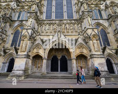 Turisti che camminano accanto alle porte e al fronte occidentale, alla cattedrale di Salisbury, Salisbury, Wiltshire, Inghilterra, REGNO UNITO, REGNO UNITO. Foto Stock