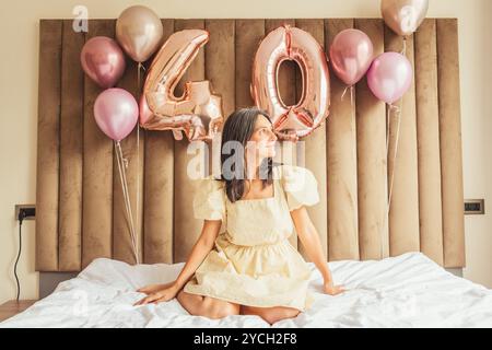 Primo piano bella matura naturale aspetto felice sottile donna caucasica festeggia gli anni '40 sdraiati in posa sul letto per la festa di compleanno indossa un abito giallo che guarda fuori Foto Stock