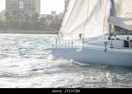 Primo piano della prua di uno yacht da corsa che attraversa l'acqua con lo skyline della città sullo sfondo al tramonto Foto Stock