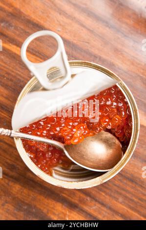 Caviale rosso in banca con cucchiaio su legno Foto Stock