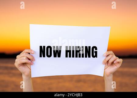 Ora è in corso l'assunzione di un messaggio scritto su carta bianca con sfondo sfocato sul lago. Simbolo di assunzione concettuale. Copia spazio. Foto Stock