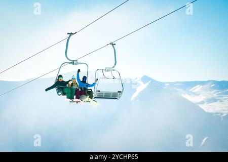 un gruppo di allegri tre amici si solleva sullo skilift per sciare e fare snowboard nella località sciistica delle montagne innevate Foto Stock