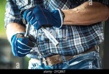 Una persona è impegnata nella riparazione dell'attrezzatura, tenendo in mano una chiave e un cacciavite, indossando guanti protettivi in un'officina ben illuminata. Foto Stock