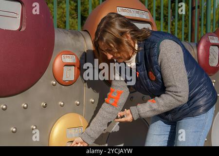 Una donna sta guardando una macchina con un cerchio rosso e oro sopra. Indossa una giacca blu e un jeans Foto Stock