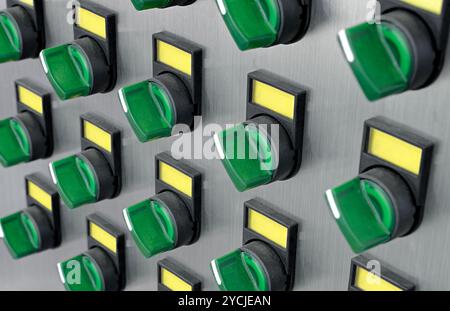 Molti interruttori elettrici verdi con etichette gialle su un pannello di controllo in metallo spazzolato. Background industriale astratto. Foto Stock