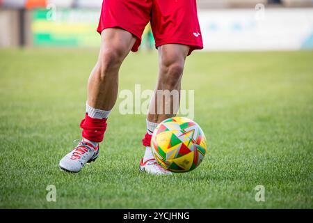 Un giocatore di calcio gambe e piedi che giocano con un calcio, mostrando pantaloncini rossi e calze e scarpe da calcio grigie e arancioni. Credito John Rose/Alamy Foto Stock