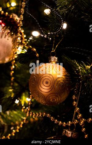Un ornamento dorato adornato da intricati disegni appesi su un albero di Natale, circondato da luci calde e decorazioni festose. Cattura l'essenza di Foto Stock