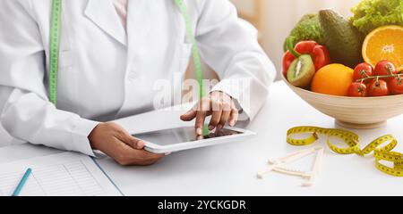 Donna nera dietista che lavora con tablet digitale in clinica Foto Stock